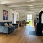 Wohnzimmer mit Sofa, Esstisch und Kaminofen. Holzboden und weiße Wände.