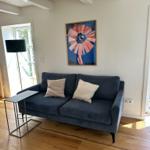 Ein dunkelblaues Sofa mit zwei Kissen steht auf Holzdielen vor einer Wand mit einem Bild.