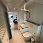 Badezimmer mit Dusche, Waschbecken und Toilette. Durchgang ins Wohnzimmer.