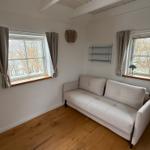 Ein Raum mit Sofa, zwei Fenstern und Holzboden.