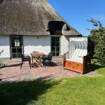 Haus mit Strohdach, Terrasse mit Tisch, Stühlen und Strandkorb.