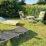 Garden with loungers, two chairs, and table. Background: green hedge.