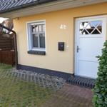 Haus mit gelber Fassade, weißer Tür und gepflastertem Vorgarten.
