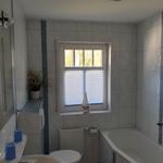 Badezimmer mit Badewanne, Toilette und Waschbecken. Fenster mit Jalousie und Segelboot-Dekoration.