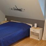Schlafzimmer mit Dachschräge, Bett und Nachttisch. Wandbild zeigt Leuchtturm und Segelboote.