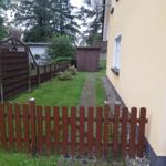 Hinterhof mit Rasen, Pflasterweg und Holzzaun. Hauswand und Garten sind sichtbar.