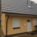 Gelbes Einfamilienhaus mit grauem Satteldach und weißer Eingangstür.