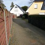 Pflasterweg zwischen zwei Häusern mit Zaun und Hecke