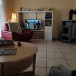 Wohnzimmer mit rotem Sessel, TV und Kaminofen. Tisch mit Schale und Fernbedienung.