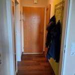 Flur mit Holzboden, gelber Wand und Garderobe mit Jacken.