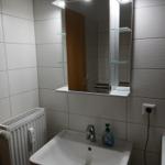 Bad mit Spiegel, Waschbecken und Heizkörper an der Wand.