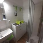 Badezimmer mit Dusche, Waschbecken und grünen Körben.