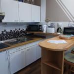 Küche mit Arbeitsplatte, Spüle und Küchenschränken. Holzbar mit Stühlen.