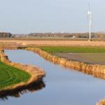 Fluss durch Felder mit Windrad im Hintergrund