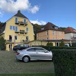 Gelbes Haus mit Balkonen und gepflastertem Hof mit parkenden Autos.