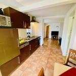 Küche mit dunklen Schränken und Terrakottaboden. Blick in Wohnzimmer mit Fernseher.