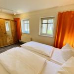 Zimmer mit zwei Betten, Holzschrank und Fenstern mit orangefarbenen Vorhängen.