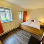 Schlafzimmer mit Doppelbett, Holzboden und Fenstern mit Vorhängen.