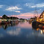 Hafen bei Sonnenuntergang mit Booten und beleuchteten Gebäuden.