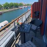 Terrasse mit Tisch, Stühlen und Blick auf den Hafen.