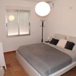 Schlafzimmer mit Bett, Nachttisch und Fenster mit Jalousie.