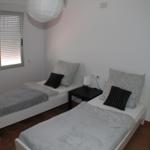 Zwei Einzelbetten mit Kissen und Decken, kleiner Nachttisch und Fenster mit Jalousien.