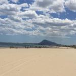 Weiterer Strand mit Sand, Meer und Berg im Hintergrund.