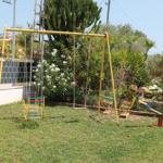 Hinterhof mit Spielplatz, Schaukel und Klettergerüst. Grasfläche und tropische Pflanzen.