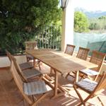 Terrasse mit Holztisch und Stühlen, Blick auf grüne Landschaft und Berge.