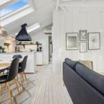 Living and dining area with kitchen under sloped ceilings and large windows.
