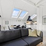 Living area with sofa, dining table, and kitchen under sloped ceilings with skylights.