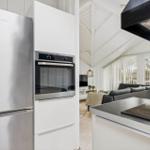 Modern kitchen with refrigerator and oven. View into living area with sofa and windows.