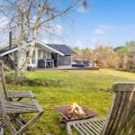 House with garden, wooden chairs, and fire pit in foreground.