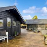Black wooden cabin with large wooden terrace, garden furniture, and view of forest.