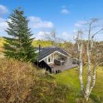 Modern wooden cabin with terrace, surrounded by trees and grass.