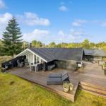 Modern villa with large wooden terrace, garden furniture, and view of forest.