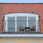 Roof terrace with table and two chairs under red tiled roof.