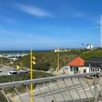 Sea, dunes, and a sailboat on a hill overlooking a beach.