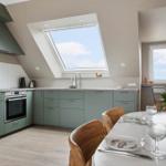 Kitchen with dining area, sloped ceiling, and windows. Wooden chairs and table with flowers.
