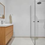Bathroom with shower, sink, and mirror. Wooden vanity and white tiles.