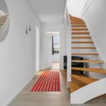 Hallway with wooden staircase, mirror, and rug