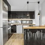 Modern kitchen with dining area, wooden floor, and black cabinets.