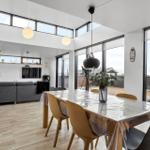 Dining area with table and chairs, living room with sofa and TV, large windows and terrace.