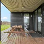 Deck with wooden table and benches, view of grass and sky.