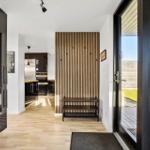 Entryway with wooden floor, wood panel wall, and view into the kitchen.