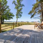 Holzterrasse mit Tisch und Stühlen, Blick auf Grünfläche und See.