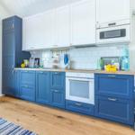 Küche mit blauen und weißen Schränken, Holzboden und weißer Fliesenwand.