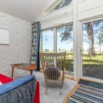Ein Raum mit rotem Sofa, Holzstuhl und großem Fenster zur Außenterrasse.