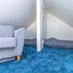 Zimmer mit grauem Sofa, blauem Teppich und Bett unter Dachschrägen.