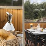 Terrasse mit Tisch, Stühlen und Brotkorb. Hintergrund: Holzzaun und Wald.